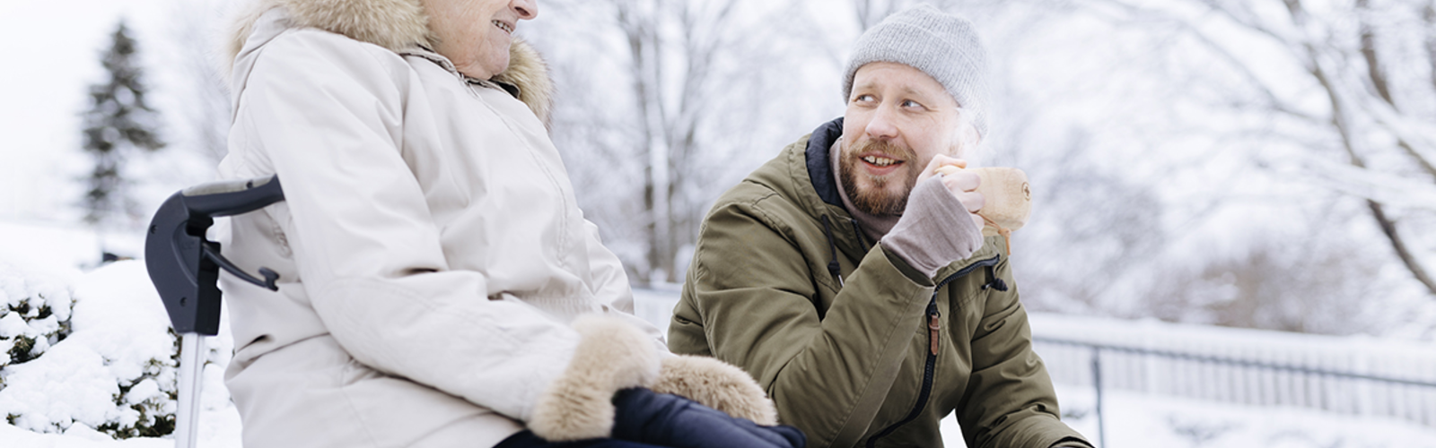 Kaksi henkilöä istuu ulkona talvisessa maisemassa juomassa kaakaota ja juttelemassa.