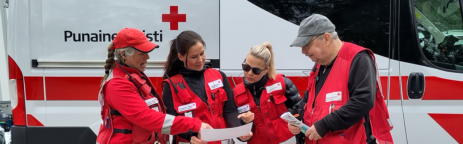 Neljä vapaaehtoista lukee paperia. Taustalla on ambulanssi.